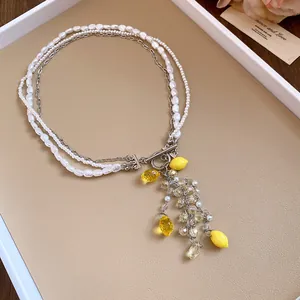 Detailed view of a layered pearl necklace with yellow resin lemon and crystal charms.