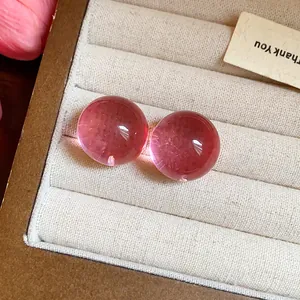 Dettaglio macro di orecchini a bottone tondi in resina rosa traslucida in scatola.
