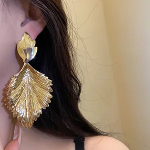 Close-up detail of oversized gold leaf drop earrings with wrinkled texture