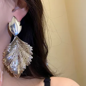 Macro detail of oversized silver leaf earrings showing metallic texture and scale
