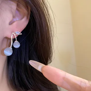 Close-up of elegant silver cherry earrings with cat-eye stones and zircon detail on model.