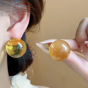 Dettaglio di orecchini a perno tondi in resina ambra traslucida con perno in argento.