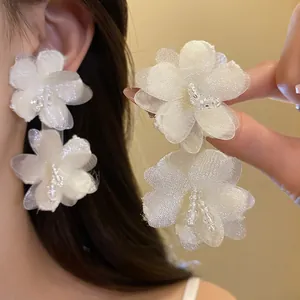 Detail of elegant white mesh flower earrings with delicate beaded centers on model