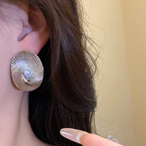 Detail view of oval textured silver-tone stud earring with pearl center worn on ear