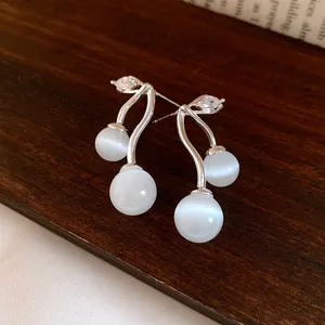 Close-up detail of elegant cherry-shaped earrings with white cat eye stones and zircons