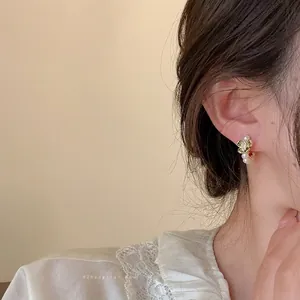 Detailed view of floral pearl earrings worn by a model, featuring green enamel and gold finish.