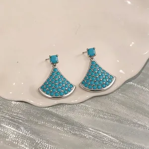 Elegant silver fan-shaped earrings featuring blue stones displayed on a white ceramic plate.