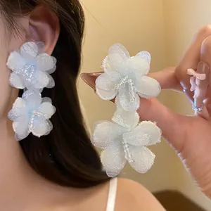 Detail shot of white and blue fabric flower earrings with beaded center