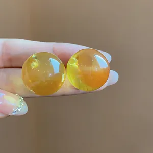 Primo piano di orecchini a lobo sferici in resina giallo miele traslucida in mano.