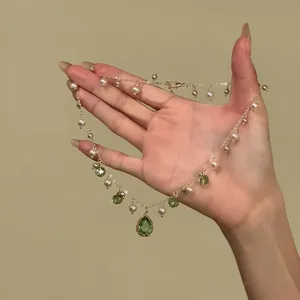Close-up detail of an elegant pearl necklace with green teardrop pendants and gold chain.