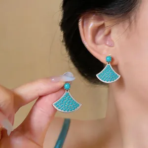 Close-up detail of elegant turquoise fan-shaped earrings worn by an Asian model.