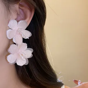 Detailed view of delicate pink fabric flower earrings with bead center worn on model's ear