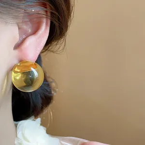 Primo piano di orecchini a bottone tondi in resina ambra traslucida sull'orecchio