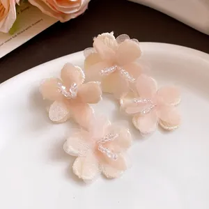 Detailed view of soft pink fabric flower stud earrings with delicate beaded centers.