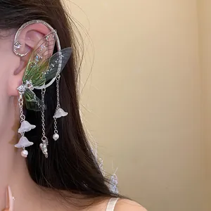 Detail view of a fairy-inspired green resin wing ear cuff with white flower pendants.