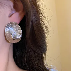 Close-up view of a golden textured round earring with a center pearl worn by a model