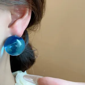 Primo piano dettagliato di un orecchino a bottone tondo in resina blu sull'orecchio di una persona