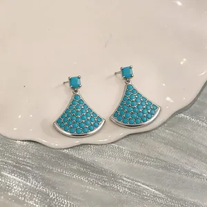 Close-up of fan-shaped silver drop earrings with turquoise stones on white ceramic plate