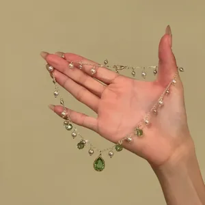 Detailed view of a gold-tone necklace with pearls and green teardrop pendants held by hand