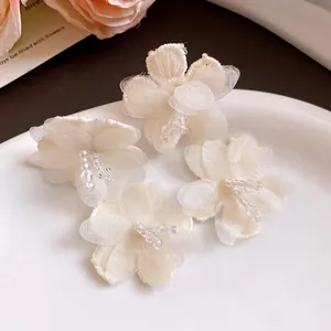 Macro detail of elegant cream fabric flower earrings with delicate bead stamens.