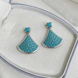 Elegant fan-shaped silver stud earrings with turquoise blue zircons in a jewelry box.