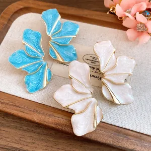 Close-up of blue and pearlescent white enamel flower petal earrings on a wooden tray