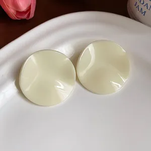 Close-up of elegant creamy-white round acrylic wrinkled stud earrings on white plate