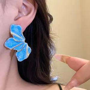 Close-up detail of oversized blue enamel flower earrings with elegant gold trim.
