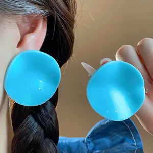 Detail shot showing vibrant blue oversized wavy acrylic stud earrings on model's ear