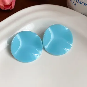Detailed view of sky blue round crimped acrylic stud earrings on a white ceramic plate