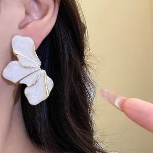 Detail showing a large white floral earring with gold border on model's ear