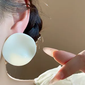 Close-up detail of oversized white acrylic wrinkled round stud earrings worn on ear