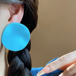 Macro detail of large bright blue irregular acrylic round stud earring worn on ear