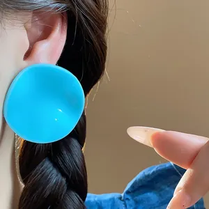 Bold vibrant blue acrylic stud earring with irregular curved design shown on model's ear