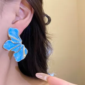 Close-up of blue floral earrings with gold trim on an ear, vintage niche jewelry design