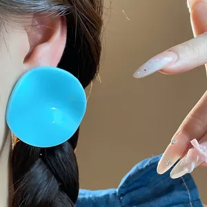 Close-up of bright blue acrylic round pleated stud earring worn on ear