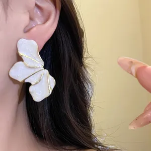 Close-up view of a large white flower petal earring with gold trim worn on an ear.