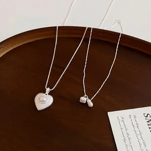 Elegant minimalist silver peanut and pearl heart pendant necklace set on wooden tray