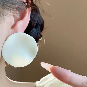 Detailed view of large white acrylic wrinkled round stud earrings worn by an Asian model