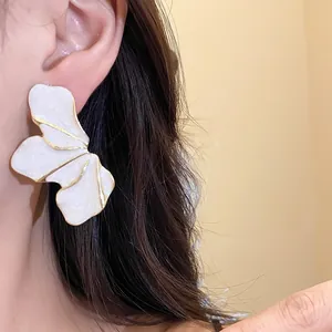 Detailed close-up view of elegant large pearl white flower petal earrings with golden edge on model