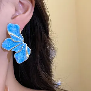 Detailed view of an elegant blue enamel floral earring with gold trim on the ear