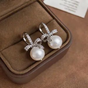 Primo piano di eleganti orecchini a fiocco in argento con zirconi pavé e pendenti di perle.