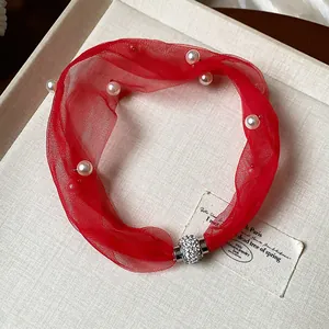 Vista dettagliata di un girocollo in rete rossa con perle e chiusura magnetica con strass