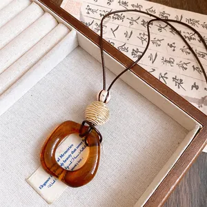 Detail of amber resin oval pendant necklace with woven bead on brown leather cord
