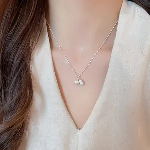 Close-up detail of a silver necklace with a delicate pearl and peanut-shaped charm.