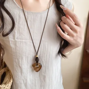Close-up of a resin oval pendant necklace with a brown leather cord on a linen top