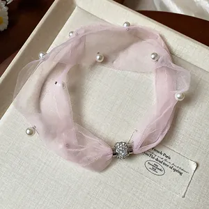 Dettaglio di collana girocollo in rete rosa con perle e chiusura magnetica