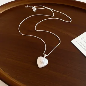 Detailed shot of a silver heart-shaped pendant with a center pearl on a box chain