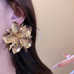 Detailed close-up view of a large metallic gold flower earring worn on a model's ear