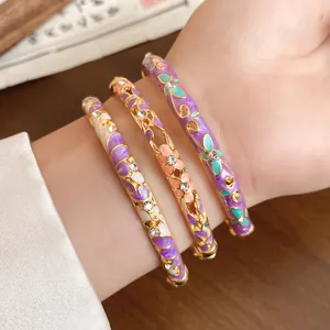 Close-up of vintage gold-plated bangles featuring colorful enamel flower patterns and crystals